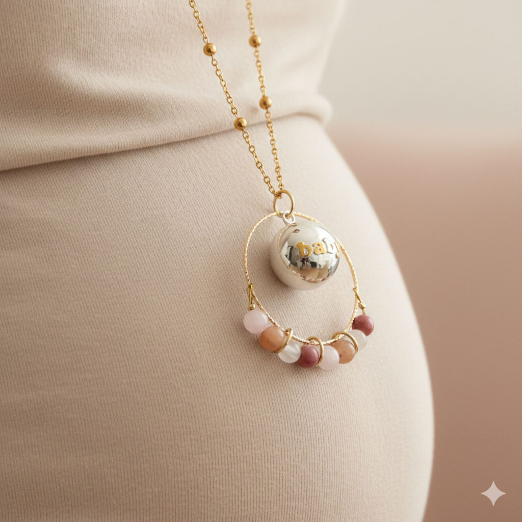 Gros plan sur le bola Baby : cercle martelé doré, boule argentée « baby » et perles naturelles aux teintes douces.